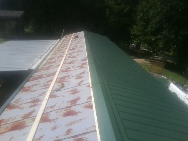 Old rusted panels beside newly installed green metal roofing — Wind Damage Roof Repair by Roofing Brothers in Rogers